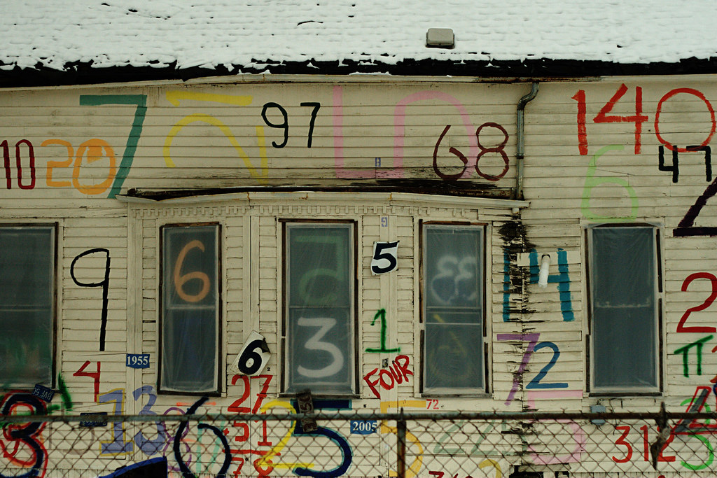 Photo of a worn house with random colored numbers hand-painted on the side